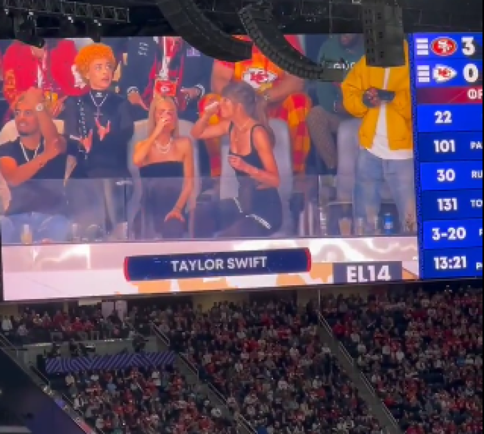 Taylor Swift and friend chug their drinks at Super Bowl LVIII in Las Vegas, Nevada, on Feb. 11, 2024. Rapper Ice Spice (orange hair) throws up hand gestures some believe to be demonic. 