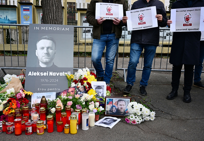 People stand next to a makeshift memorial of flowers and candles for Kremlin critic Alexei Navalny at the Russian embassy in Bucharest, Romania, on February 18, 2024. Alexei Navalny's supporters accused Russian authorities of being 'killers' who were 'covering their tracks' by refusing to hand over his body, as the Kremlin stayed silent despite Western accusations and a flood of tributes to the late opposition leader. Tributes continued to pour in, as supporters staged anti-Putin protests and pop-up tributes to Navalny around the world. Navalny's death was announced on February 16, 2024, after three years in detention and a poisoning that he blamed on the Kremlin. 
