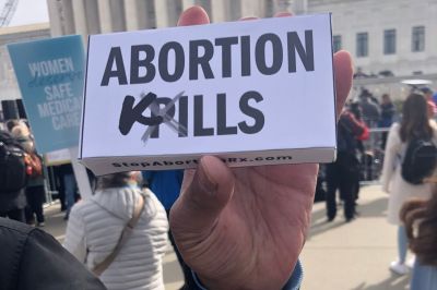 Pro-Life San Francisco Executive Coordinator Robert Byrd holds up a fake abortion pill box designed by PAAU outside of the U.S. Supreme Court during oral arguments for FDA v. Alliance for Hippocratic Medicine on March 26, 2024. The box, designed by PAAU, reads 'Abortion Kills.'