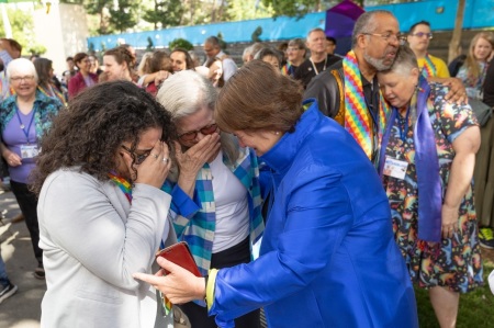 Bishop Karen Oliveto (in blue jacket) and her wife, Robin Ridenour (front, center) join in embracing delegates and visitors t the 2024 United Methodist General Conference in Charlotte, N.C., after the conference voted to remove the denomination’s ban on the ordination of clergy who are “self-avowed practicing homosexuals” — a prohibition that dates to 1984.