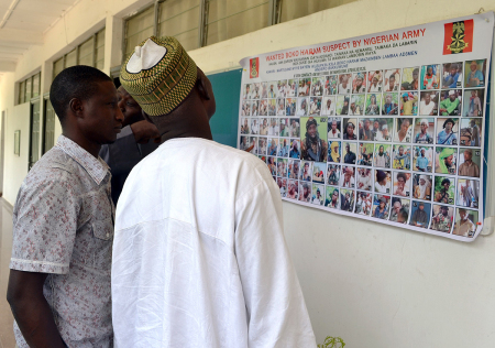 People look at a poster in Maiduguri on October 28, 2015 displaying one hundred Boko Haram suspects declared wanted by the Nigerian army.