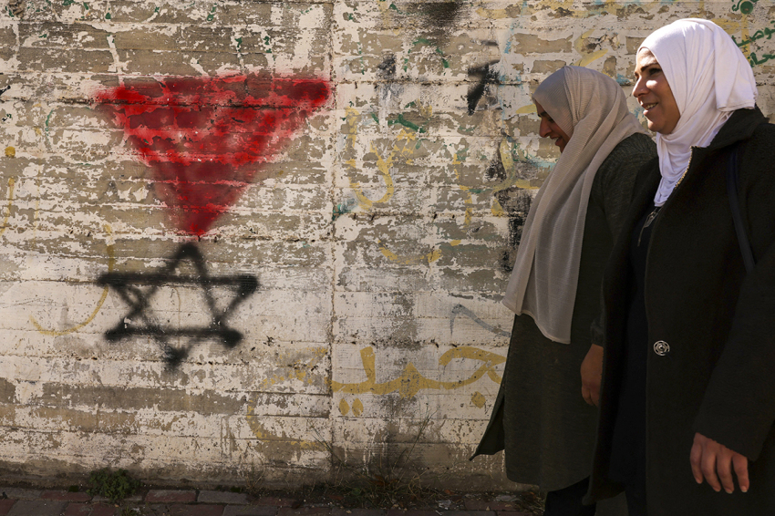 Palestinian women walk past a graffiti of the Star of David under an inverted