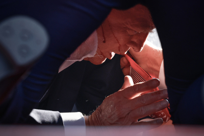 Republican presidential candidate former President Donald Trump is shown covered by U.S. Secret Service agents after an assassination attempt on his life during a rally on July 13, 2024, in Butler, Pennsylvania. Butler County district attorney Richard Goldinger said the shooter is dead after injuring former U.S. President Donald Trump, killing one audience member and injuring another in the shooting. 