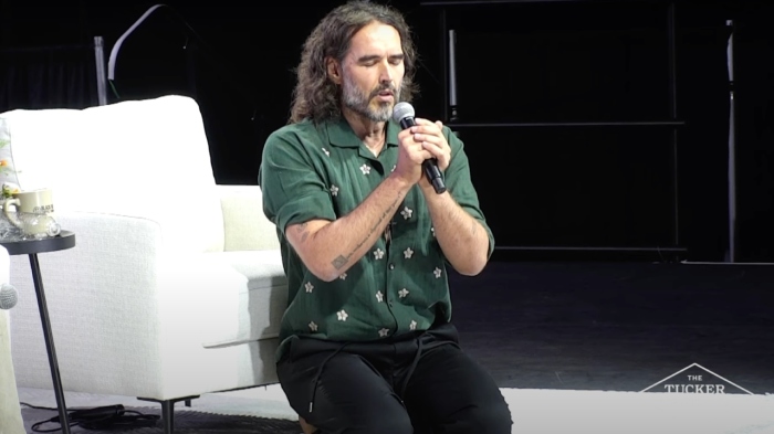 A barefoot Russell Brand kneels in prayer at the conclusion of his conversation with Tucker Carlson during at event with the former Fox News host in Phoenix, Arizona, on Sept. 4, 2024.