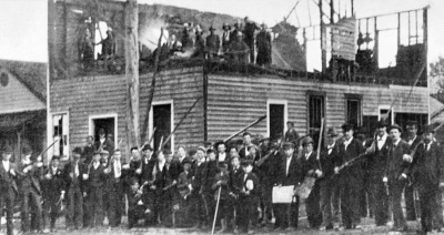 Armed rioters in front of a burned-down press building amid an event commonly called the "Wilmington Coup" or "Wilmington Massacre," which occurred in Wilmington, Delaware, in 1898.