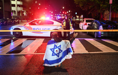 A man draped in the Israeli flag, bearing a cross and the name "Jesus" at its center, gestures as Metropolitan Police officers secure the area outside the Capital Jewish Museum following a shooting that left two people dead in Washington, D.C., in the early hours of May 22, 2025. Two Israeli embassy staffers were shot dead late Wednesday, May 21, outside a Jewish museum in Washington by a gunman who shouted "free, free Palestine," authorities said, with U.S. officials and Israeli diplomats expressing shock and outrage over the killings. 