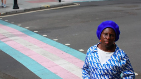 Resident Blessing Olubanjo stands in front of a pedestrian crossing in trans pride colors approved by Camden Borough Council in 2021 to honor the work of the disgraced Tavistock clinic.