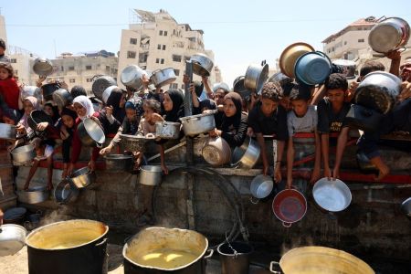 Palestinians receive lentil soup at a food distribution point in Gaza City on August 2, 2025. 