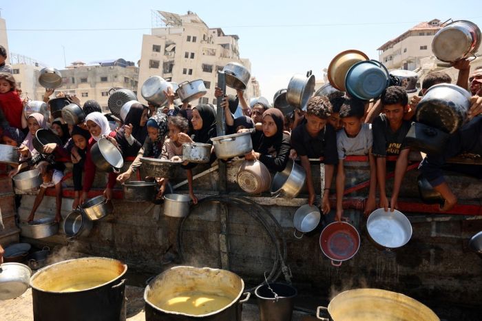 Palestinians receive lentil soup at a food distribution point in Gaza City on August 2, 2025. 