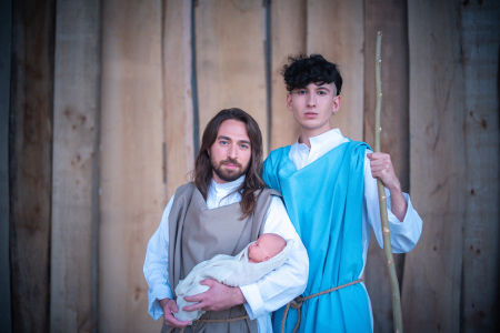Two homosexual men holding a baby and posing as biblical characters. 