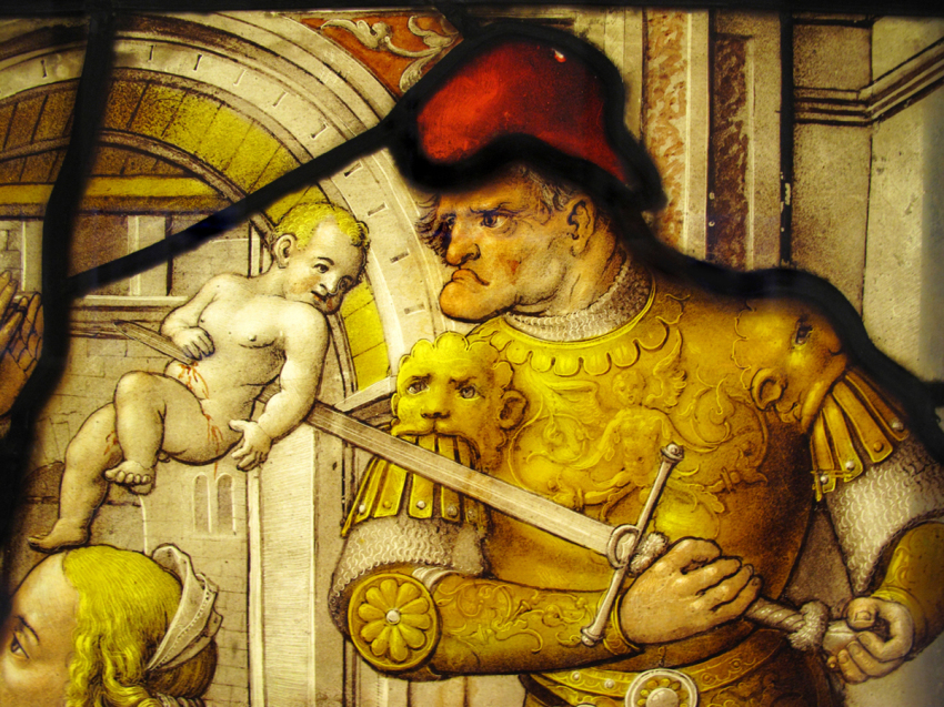 The Massacre of The Innocents from the New Testament shown in an image on a medieval 16th century stained glass window panel. The image shows a Roman soldier slaughtering a boy child on the orders of Herod, in an attempt to eliminate the Christ Child