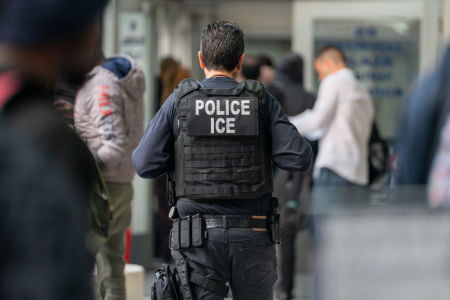 An ICE agent monitors hundreds of asylum seekers being processed upon entering the Jacob K. Javits Federal Building on June 6, 2023 in New York City. New York City has provided sanctuary to over 46,000 asylum seekers since 2013, when the city passed a law prohibiting city agencies from cooperating with federal immigration enforcement agencies unless there is a warrant for the person's arrest.
