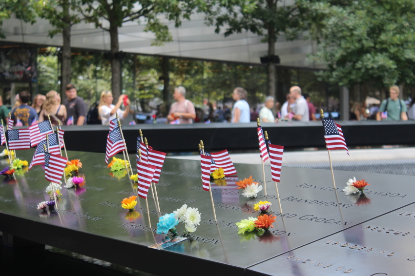 Tourists observe multiple flags among the names of 9/11 victims on a section of the bronze parapet surrounding the south waterfall reflecting pool at the National September 11 Memorial & Museum in Lower Manhattan, New York, on Sept. 10, 2026.
