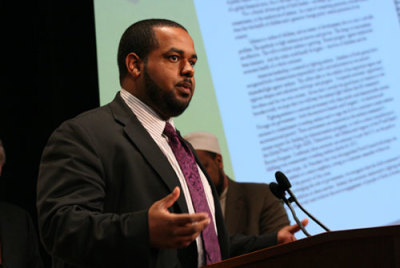 Joshua Dubois, former director for the White House Office of Faith-based and Neighborhood Partnerships, speaks at the One World Against Malaria campaign launch on Friday, April 24, 2009. On the screen in the background is a copy of the letter faith leaders presented to him to deliver to President Obama.