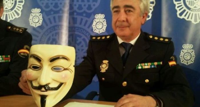Spanish police holding up 'Anonymous' prop face mask normally used by its members.