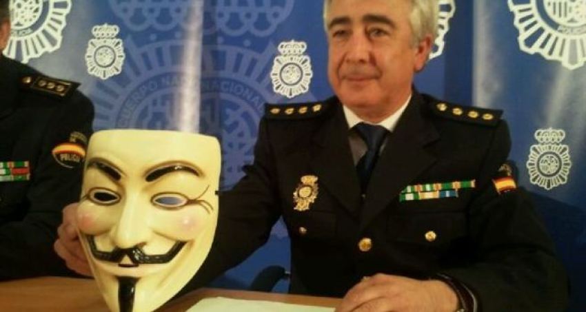 Spanish police holding up "Anonymous" prop face mask normally used by its members.