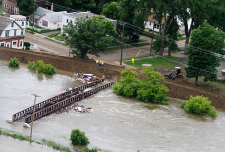 Workers inspect a flooded pedestrian walk way, as debris is trapped by the structure in Minot, North Dakota, June 24, 2011. Federal officials sharply increased plans to release more water on the swollen Souris River on Thursday, adding up to three feet to the expected peak of flooding at Minot, North Dakota, where thousands of homes already have been evacuated.