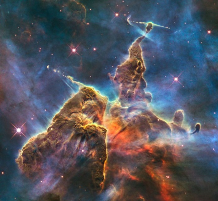A small portion of one of the largest seen star-birth regions in the galaxy, the Carina Nebula. Towers of cool hydrogen laced with dust rise from the wall of the nebula. The scene is reminiscent of Hubble's classic 'Pillars of Creation' photo from 1995, but is even more striking in appearance. The image captures the top of a three-light-year-tall pillar of gas and dust that is being eaten away by the brilliant light from nearby bright stars. The pillar is also being pushed apart from within, as infant stars buried inside it fire off jets of gas that can be seen streaming from towering peaks like arrows sailing through the air. (Caption:NASA)