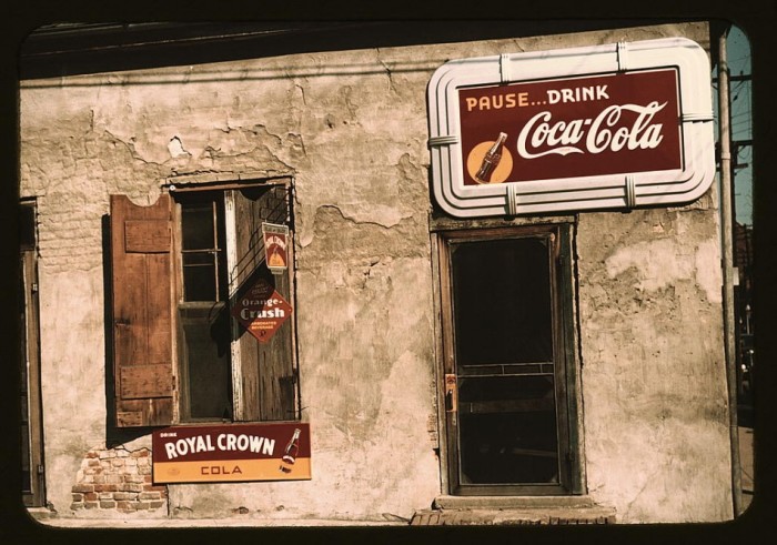 Photograph shows store or cafe with soft drink signs. Diamond-shaped sign: Fresh Orange-Crush'; above it: Relax and enjoy Royal Crown Cola.