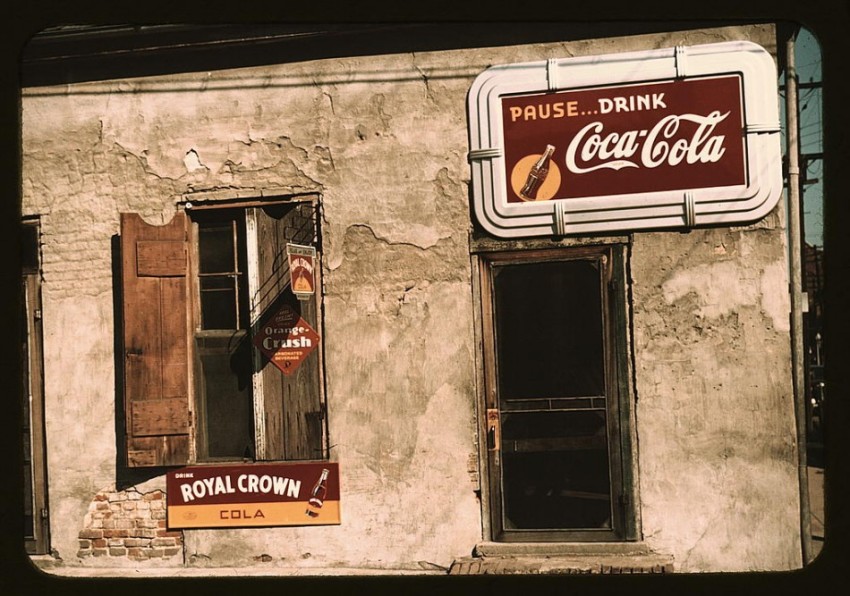 Photograph shows store or cafe with soft drink signs. Diamond-shaped sign: Fresh Orange-Crush"; above it: Relax and enjoy Royal Crown Cola.