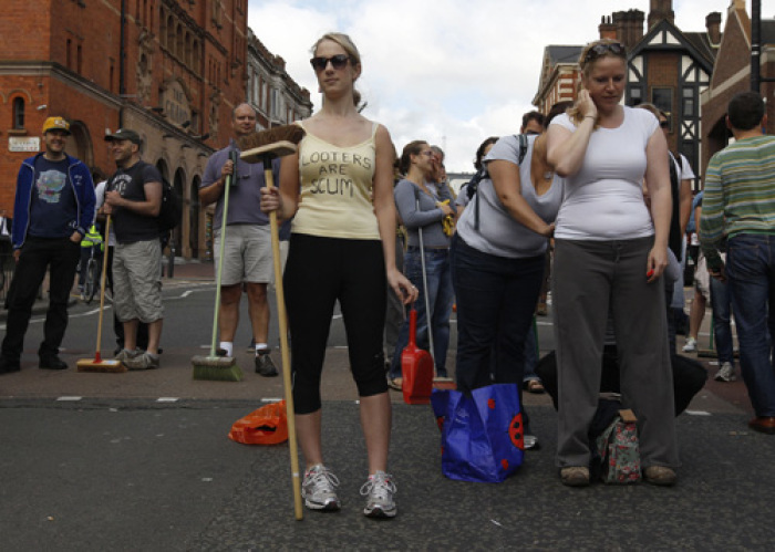 A woman poses for a photograph as volunteers wait to clear-up after overnight disturbances in Clapham Junction, in south London August 9, 2011. British Prime Minister David Cameron said he would recall parliament from its summer recess for a day on Thursday after rioting swept through London for three consecutive nights.