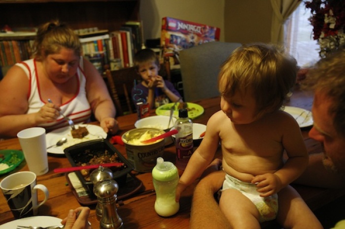 (L-R) Katie Busker, 30, and her son, Austin Spiker, 6, eat dinner as fourteen-month-old, Johnnalyn Gibbs, is propped up by her father Dustin in Independence, Iowa. Busker, who receives food stamps and is unemployed due to a disability, stays home and watches the kids while her sister and brother-in-law are at work. July 5, 2011