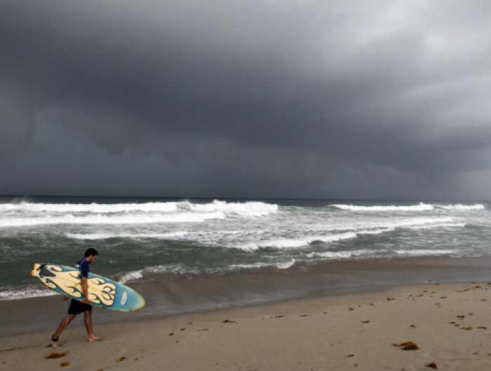A surfer walks along the beach as rain bands from Hurricane Irene passes off the Florida coastline in Deerfield Beach, Florida August 25, 2011. Hurricane Irene will affect eastern North Carolina on Saturday as a major hurricane and the U.S. eastern seaboard north from there is within its path, U.S. National Hurricane Center Director Bill Read said on Thursday.