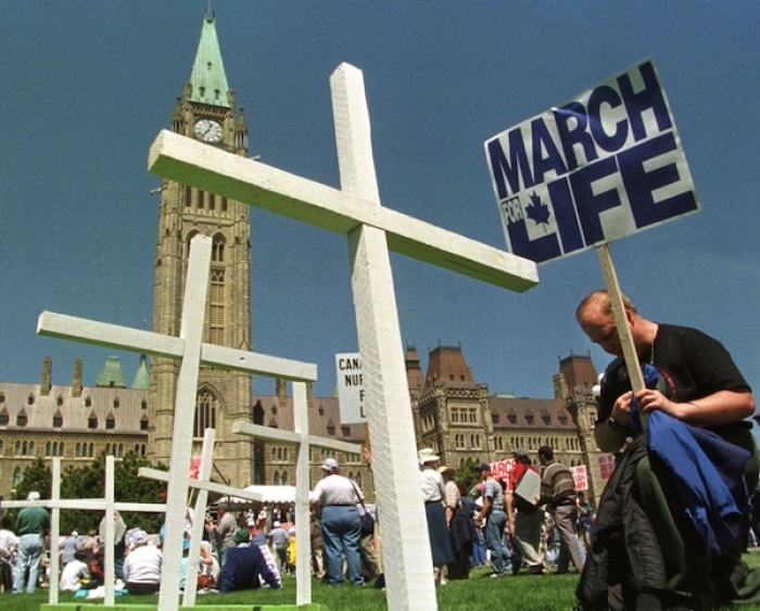 Credit : A pro-life supporter kneels down to pray in front of crosses planted on the front lawn of Parliament Hill at a rally.