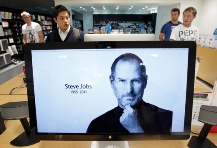 Customers look around products behind a computer monitor displaying the obituary of former Apple CEO Steve Jobs at an Apple Store in Seoul October 6, 2011. Apple Inc co-founder and former CEO Steve Jobs died on Wednesday at the age of 56, after a years-long and highly public battle with cancer and other health issues.