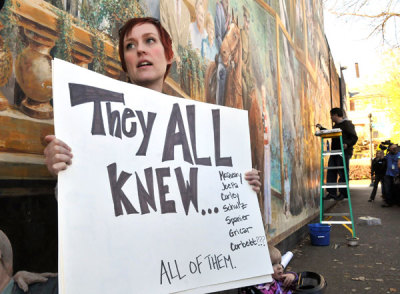 Emily Wilkens, 33, of State College, Pa., holds a sign protesting while artist Michael Pilato (R) paints over a portion of a mural that former Penn State football coach Jerry Sandusky was featured on, in this Nov. 9, 2011 file photo.