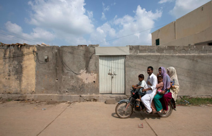 A family rides past the locked house of Rimsha Masih, a Pakistani Christian girl accused of blasphemy, on the outskirts of Islamabad on August 23, 2012. Masih, who is detained on accusations of defaming Islam, was too frightened to speak in a prison where she is being held in solitary confinement for her safety, an activist who said he visited her said on Thursday.