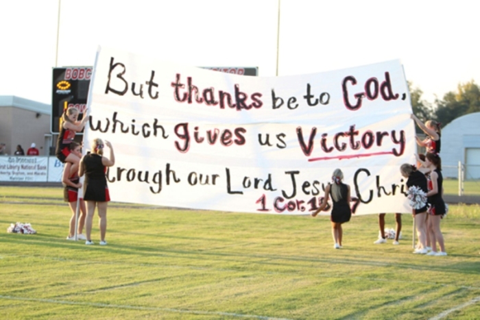 Cheerleaders from Kountze High School in Texas set up a banner covered with a Bible verse in preparation for the school's football team to take the field by running through it.