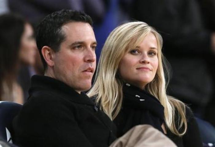 Actress Reese Witherspoon (R) and her husband Jim Toth watch the Toronto Raptors play the Los Angeles Lakers in their NBA basketball game in Los Angeles, March 8, 2013.