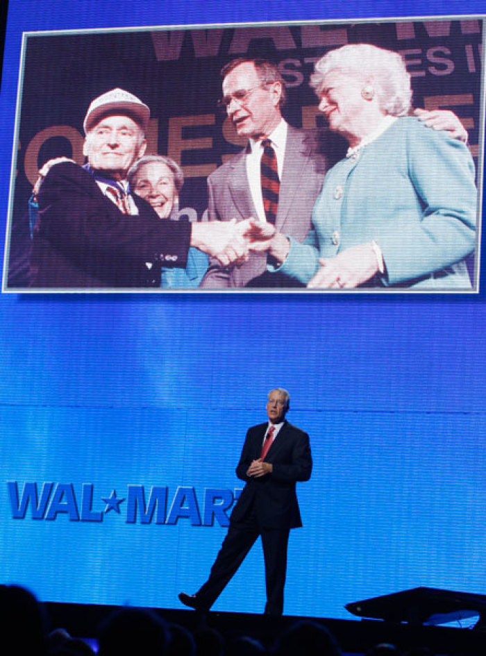 Wal-Mart Chairman of the Board Rob Walton (bottom) stands beneath a photo of his late father, Wal-Mart Founder Sam Walton, shaking hands with former US President George Bush and former First Lady Barbara Bush as he speaks to shareholders at the Wal-Mart Shareholders Meeting in Fayetteville, Arkansas June 6, 2008. Wal-Mart Stores Inc annual meeting got under way on Friday with a combination of self-congratulations for a year in which the retailer began to get its U.S. sales back on track and a tinge of nostalgia for its founder, Sam Walton.