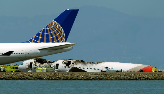 A passenger plane taxis on the runway past an Asiana Airlines Boeing 777 that crashed while landing at San Francisco International Airport in San Francisco, California July 6, 2013.