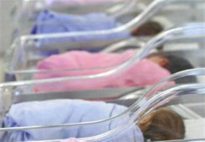 Babies wearing pink and blue blankets identifying their gender wait in the hospital.