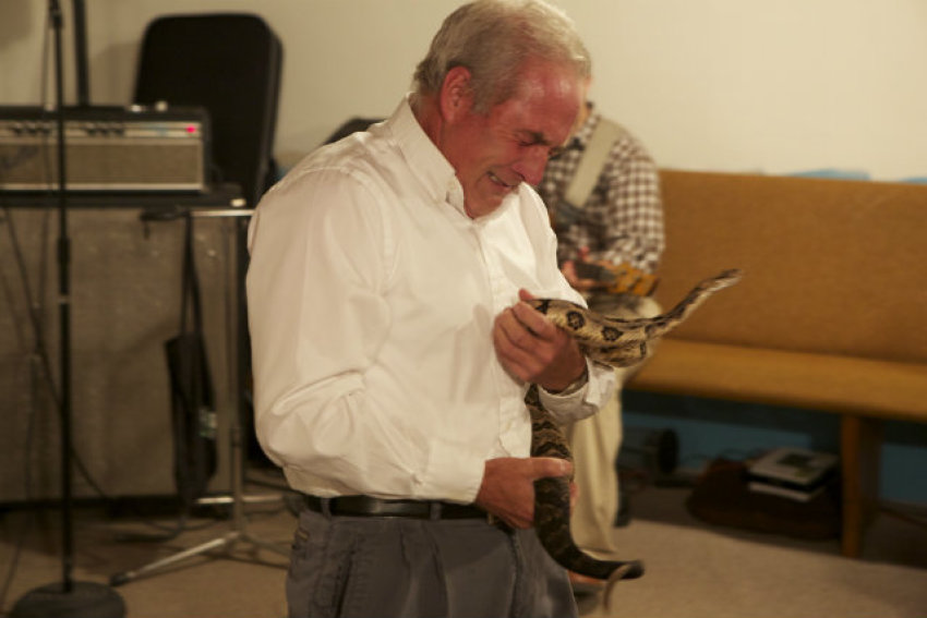A man worships holding a snake in an episode of "Snake Salvation" on National Geographic Television.