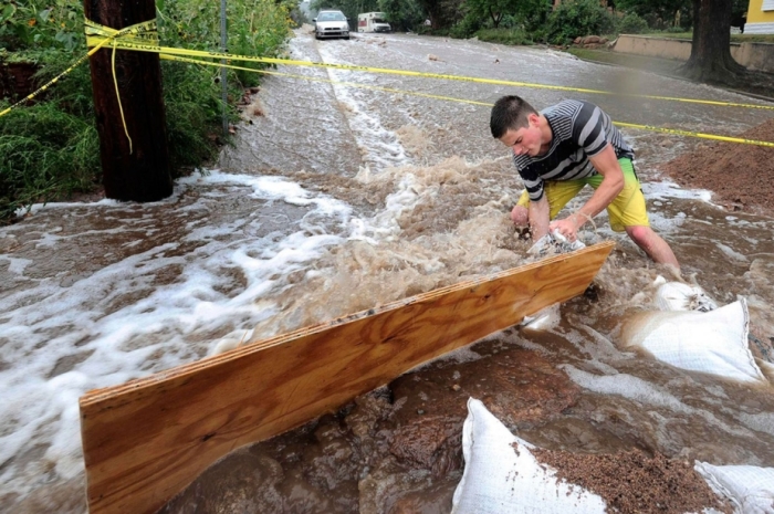 Jake Bennett drops a sand bag down to help funnel water down a street in Boulder, Colo.