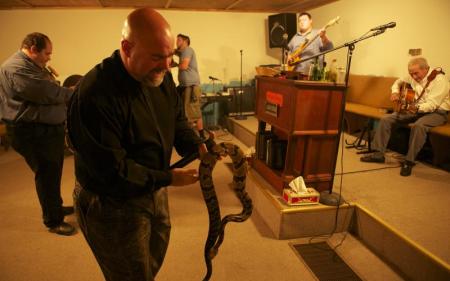 Pastor Jamie Coots holds a snake while Big Cody plays guitar in the background at his Middlesboro, Kentucky, church in an episode of "Snake Salvation" on National Geographic Television.