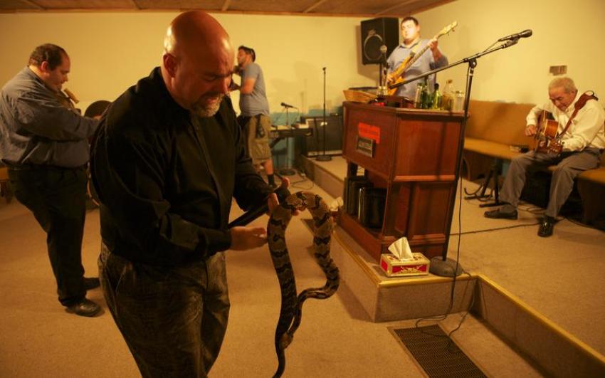 Pastor Jamie Coots holds a snake while Big Cody plays guitar in the background at his Middlesboro, Kentucky, church in an episode of "Snake Salvation" on National Geographic Television.