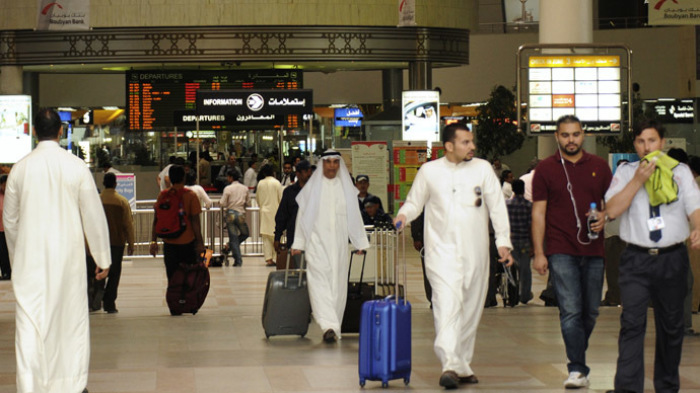 Travellers walk with their luggage at Kuwait International airport.