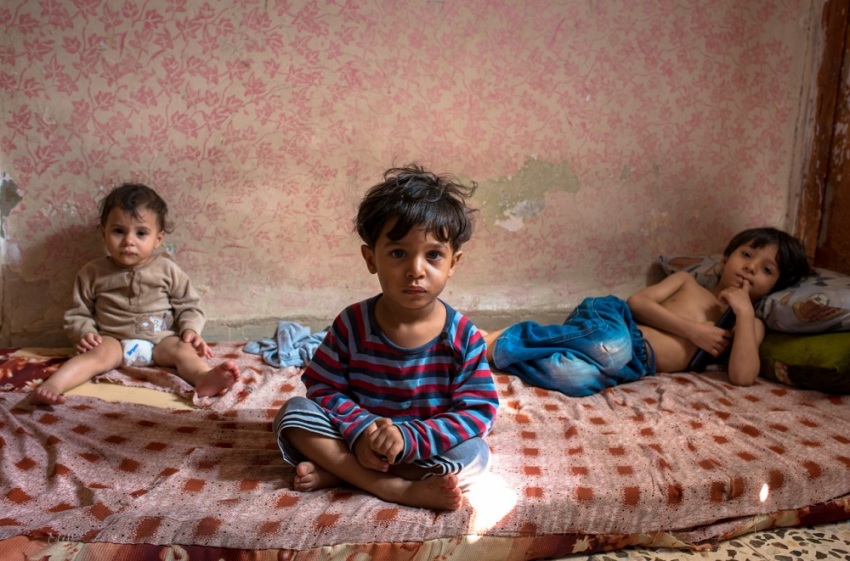 Without anywhere to go, Syrian refugee children and siblings, Adel, 5, (right), Semer, 2 (center) and Islam, 1, spend their day on the cot inside a dilapidated basement room in Jordan. Their mother says she tries to play with her children but it's not enough. 