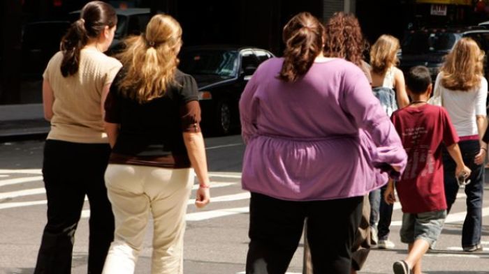 Obese pedestrians cross a street.