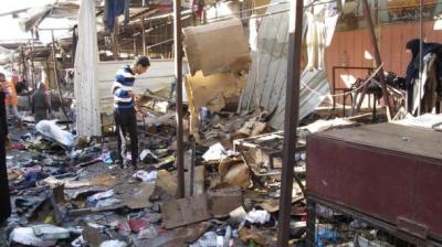 People stand among debris at the site of a bomb attack at a marketplace in Baghdad's mostly Christian Doura District December 25, 2013