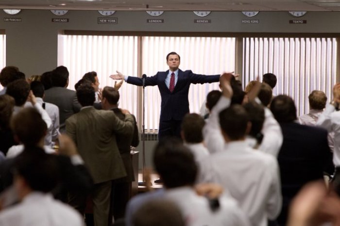 Jordan Belfort (Leonardo DiCaprio), 'The Wolf of Wall Street,' stands with his hands outstretched, declaring riches for his company through stock fraud.