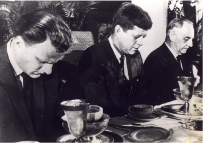 Prominent Evangelist Billy Graham prays with President John F. Kennedy. Graham biographer Hanspeter Nuesch explained that even though he rubbed shoulders with famous people, Graham did not stress fame - he even told the president to all him back because he was speaking with his maid.