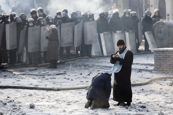 'A man kneels before an Orthodox priest in an area separating police and anti-government protesters near Dynamo Stadium on Jan. 25, 2014, in Kiev.'