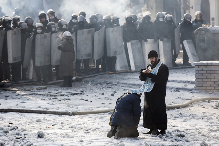 "A man kneels before an Orthodox priest in an area separating police and anti-government protesters near Dynamo Stadium on Jan. 25, 2014, in Kiev."