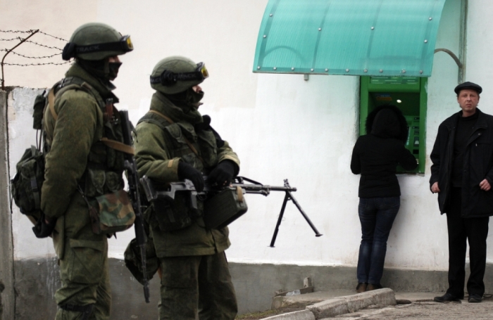 People stand near an ATM, as military personnel are seen in the foreground, outside the territory of a Ukrainian military unit in the village of Perevalnoye outside Simferopol March 2, 2014. Ukraine mobilized for war on Sunday, after Russian President Vladimir Putin declared he had the right to invade, creating the biggest confrontation between Moscow and the West since the Cold War.