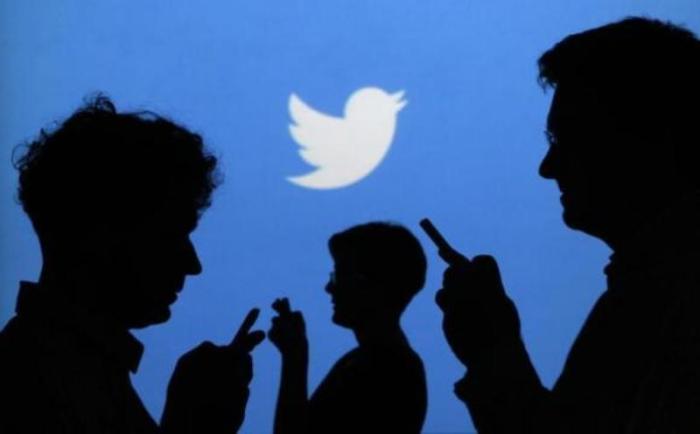 People holding mobile phones are silhouetted against a backdrop projected with the Twitter logo in this illustration picture taken in Warsaw, Poland, Sept. 27, 2013.